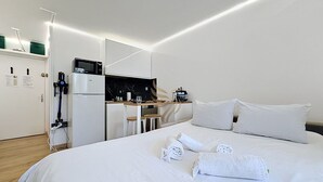 A hotel room with a bed, white linens, a desk with a computer, and a microwave. - Reflet Azur - Modern Studio with Sea View Balcony (Fréjus)