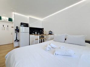 Ein Hotelzimmer mit Bett, weißen Laken, Schreibtisch mit Computer und Mikrowelle.