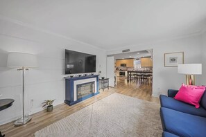 Ein modernes Wohnzimmer mit Kamin, Flachbildfernseher, Essbereich und einer Küche im Hintergrund.