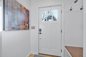 Eine weiße Tür mit Fenster darüber, ein kleiner Teppich auf dem Boden und eine Holzbank zur Rechten.