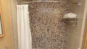 Une douche avec un mur recouvert de mosaïques, un rideau blanc et un porte-serviettes.