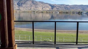 Une vue sur un lac, avec des montagnes en arrière-plan, une zone herbeuse au premier plan et une rambarde métallique.
