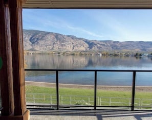 Une vue sur un lac, avec des montagnes en arrière-plan, une zone herbeuse au premier plan et une rambarde métallique.