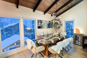 Zona pranzo con tavolo in legno, sedie bianche e un'ampia finestra vista su un paesaggio innevato.