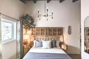 Una camera da letto con un letto grande, un lampadario, una testiera in legno, un comodino con una lampada e una finestra con tende.