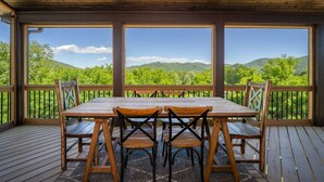 Un terrazzo in legno con tavolo e sedie, ampie finestre e vista su dolci colline.