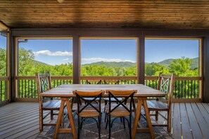 A wooden deck with a table and chairs, large windows, and a view of green hills. - Three Sisters Summit: Mountain Views, Game Room (Black Mountain)