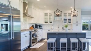 Una cucina moderna con elettrodomestici in acciaio inossidabile, mobili bianchi e un'isola centrale con sgabelli da bar.