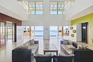 Eine großzügige Lobby mit Blick auf Pool und Meer, ausgestattet mit Korbsesseln und einem Couchtisch.
