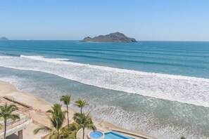 Blick auf einen Strand mit Schwimmbad, Palmen und einer entfernten Insel.