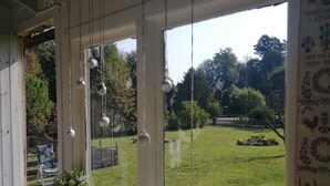 A room with a window overlooking a garden, a chair, and a potted plant. - The House of Happiness (Boda Glasbruk)