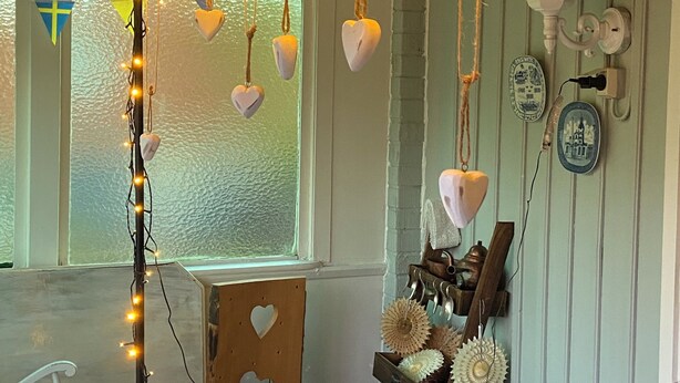 A room with a table, chairs, string lights, heart-shaped decorations, and wall-mounted items. - The House of Happiness (Boda Glasbruk)