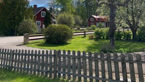 A rural setting with two red houses, a wooden fence, and a clear blue sky. - The House of Happiness (Boda Glasbruk)