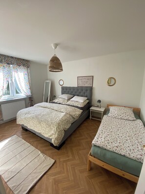 A bedroom with a large bed, a smaller bed, a bedside table, a mirror, and a hanging light fixture.