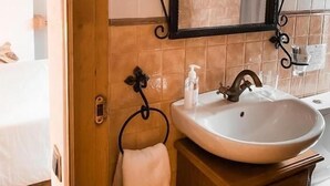 A bathroom with a wooden vanity, a white sink, a mirror with a black frame, and a towel hanging on a hook. - Casa as Fontes (Muíños)