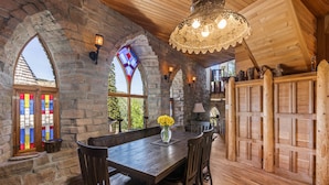 Un comedor de paredes de piedra con mobiliario de madera, una ventana de vitral y un techo de madera.