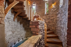 A stone-walled interior with wooden stairs and a wooden handrail.