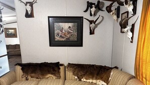 A sectional sofa with a brown and white pattern, a framed picture on the wall, and mounted animal skulls.