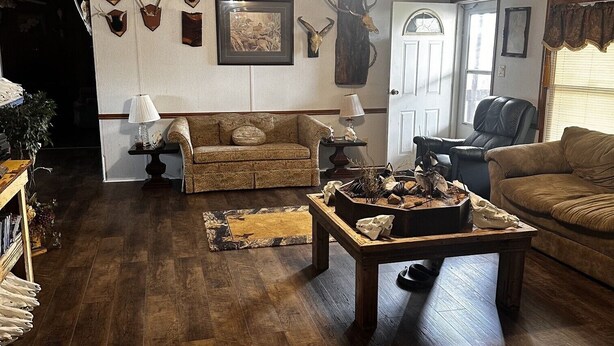 A living room with a wooden floor, two sofas, a coffee table, and wall-mounted deer skulls.