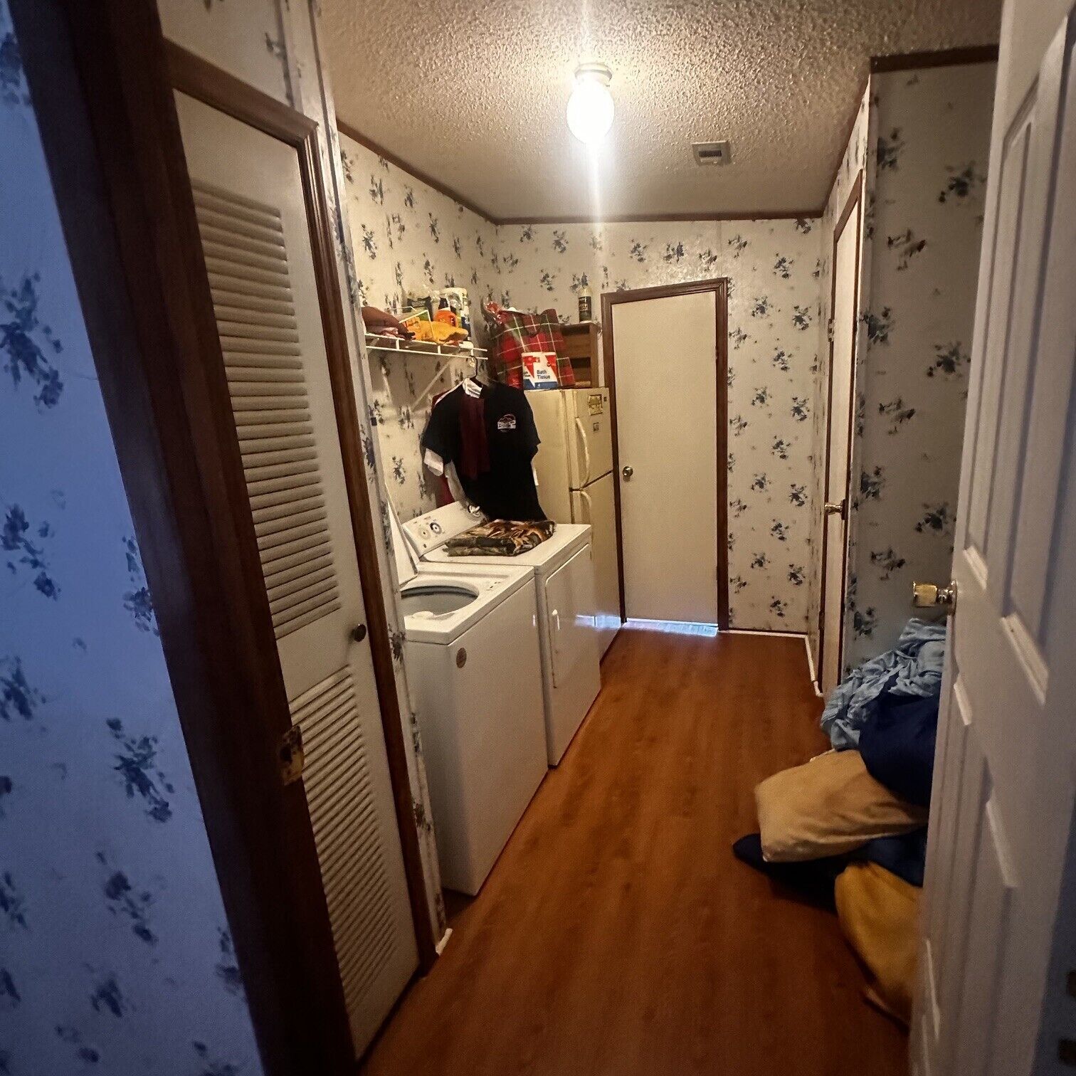 Un couloir étroit avec un lave-linge, une porte et un lit avec un oreiller.