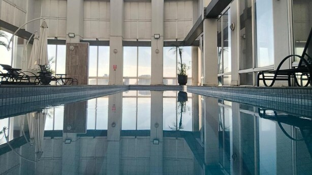 En swimmingpool med klart vand, omgivet af en bygning med store vinduer og flisegulv.