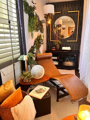 A lounge chair with a side table, a mirror, and a potted plant.