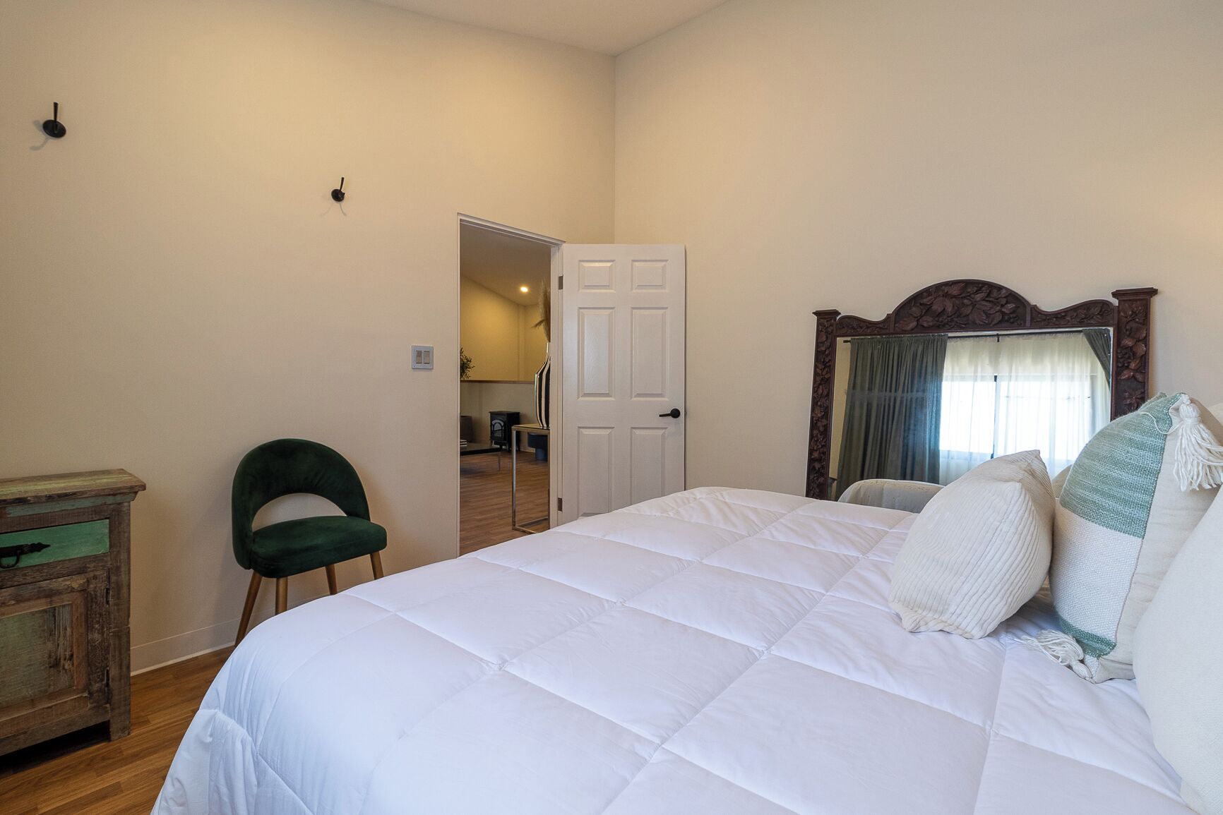 A bedroom with a bed, a chair, a dresser, and a door leading to another room.