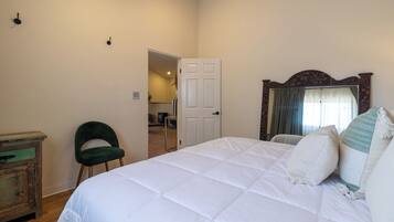 A bedroom with a bed, a chair, a dresser, and a door leading to another room.