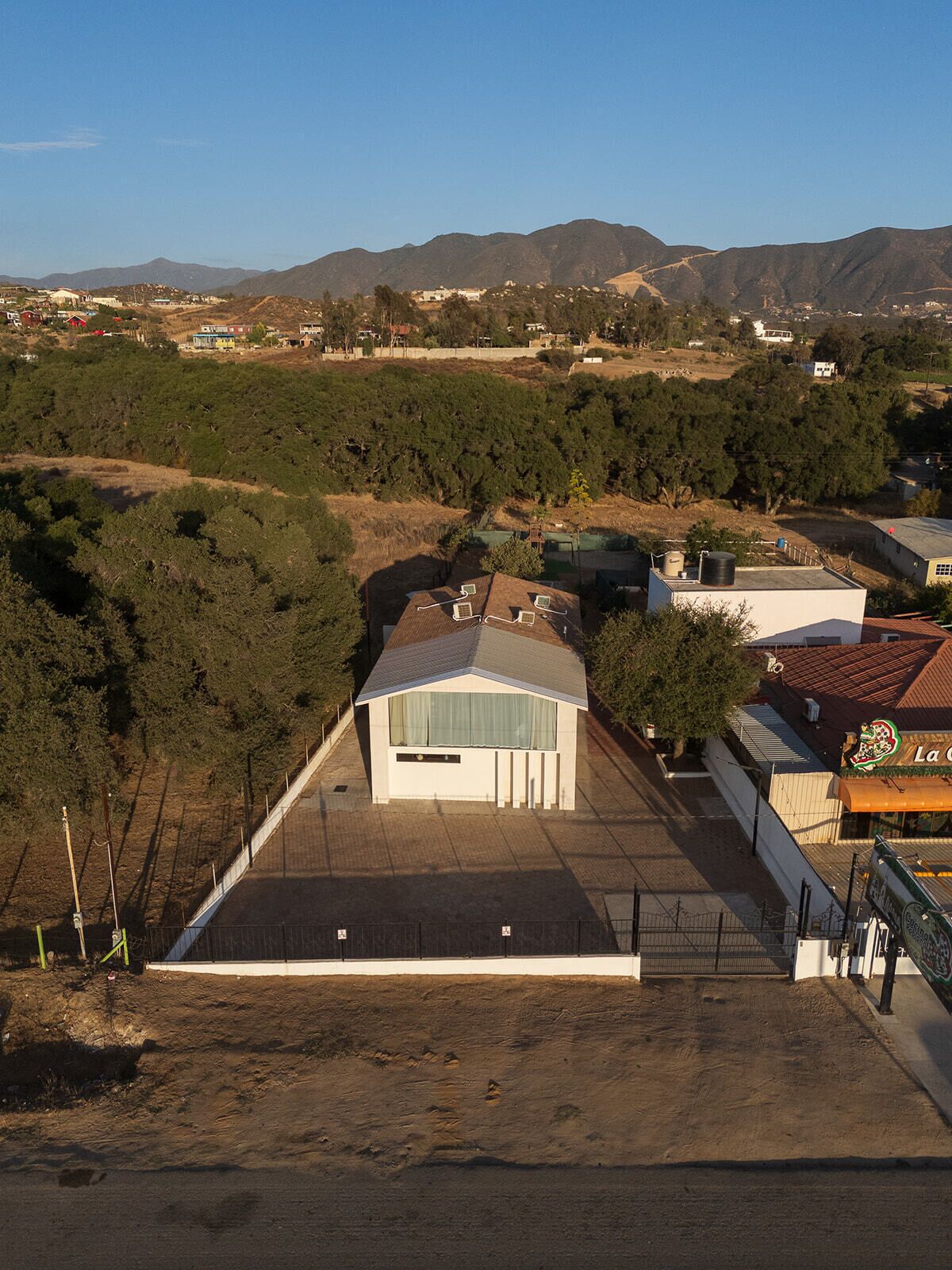 Un quartier résidentiel avec une maison dotée d’un toit en pente, d’une cour clôturée et offrant une vue sur les montagnes lointaines.