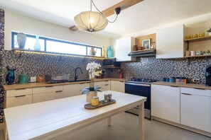 Una cocina moderna con encimera blanca, una mesa de comedor y un salpicadero de azulejos pequeños.