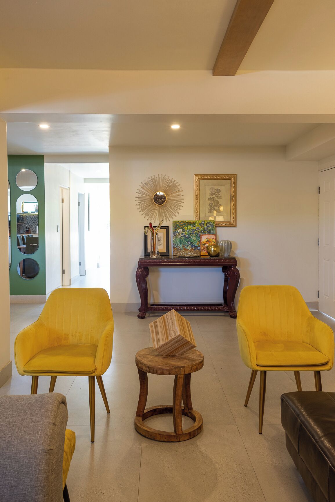 A living room with two yellow armchairs, a small wooden table, a fireplace, and a mirror on the wall.