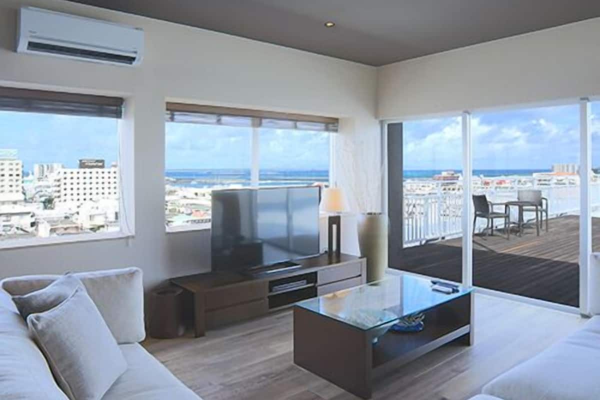 A modern living room with a sofa, TV, and a balcony with a view of the city.