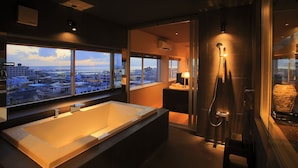 A modern bathroom with a large bathtub, a shower, and a view of the city through large windows. - Grand Villa Cucule Ishigaki Island (Ishigaki)