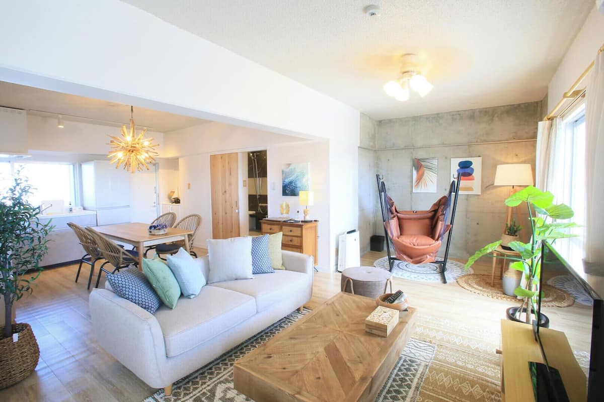 A modern living room with a sofa, coffee table, and a hanging chair. There is a dining area with chairs and a table.