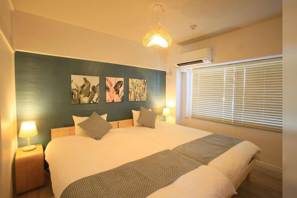 A bedroom with a bed, bedside lamps, a window with blinds, and wall art.