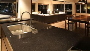 A modern kitchen with a central island, a dining area with a table and chairs, and a view of the city at night. - Grand Villa Cucule Ishigaki Island (Ishigaki)