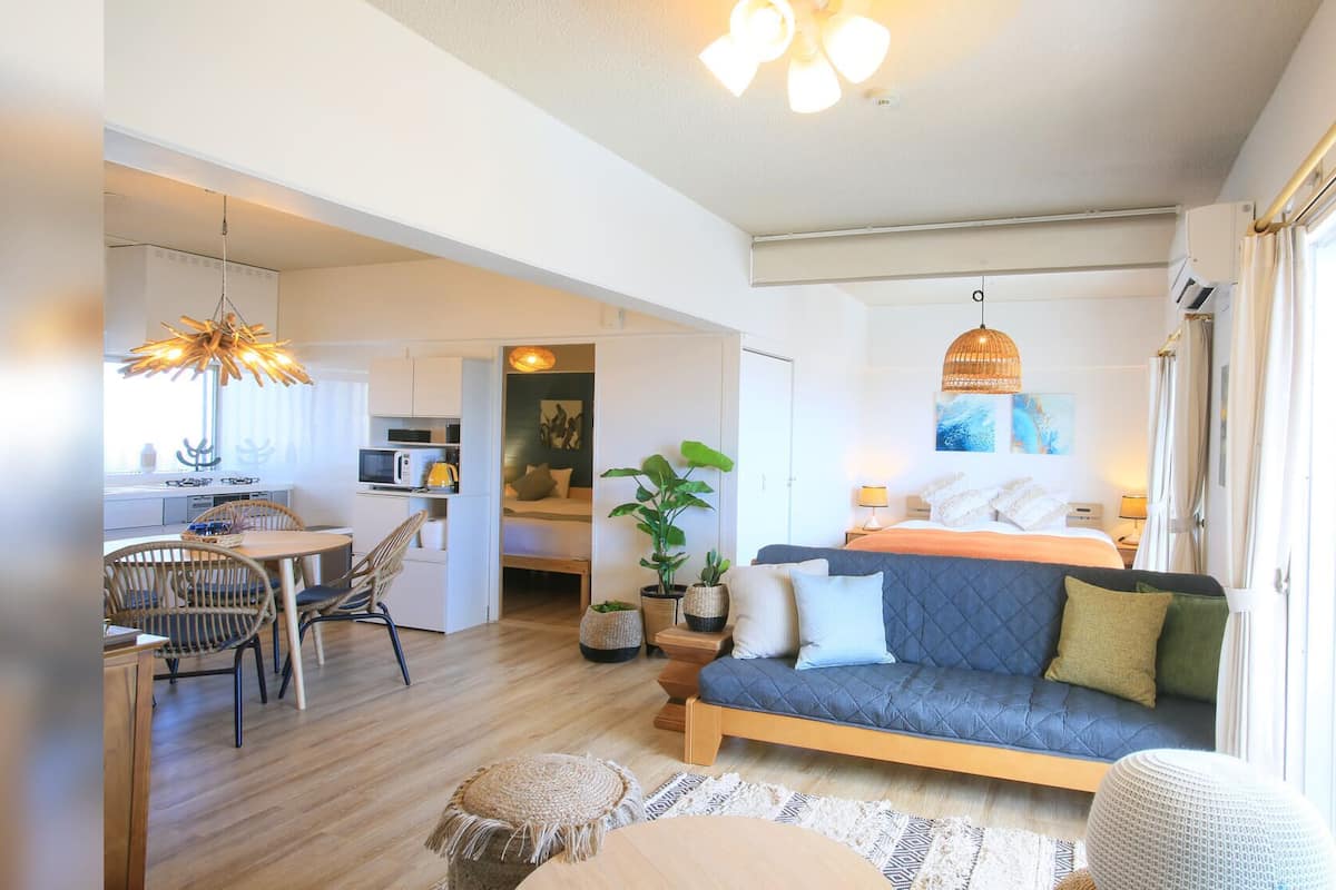 A compact, well-lit room with a bed, seating area, kitchenette, and a dining table.