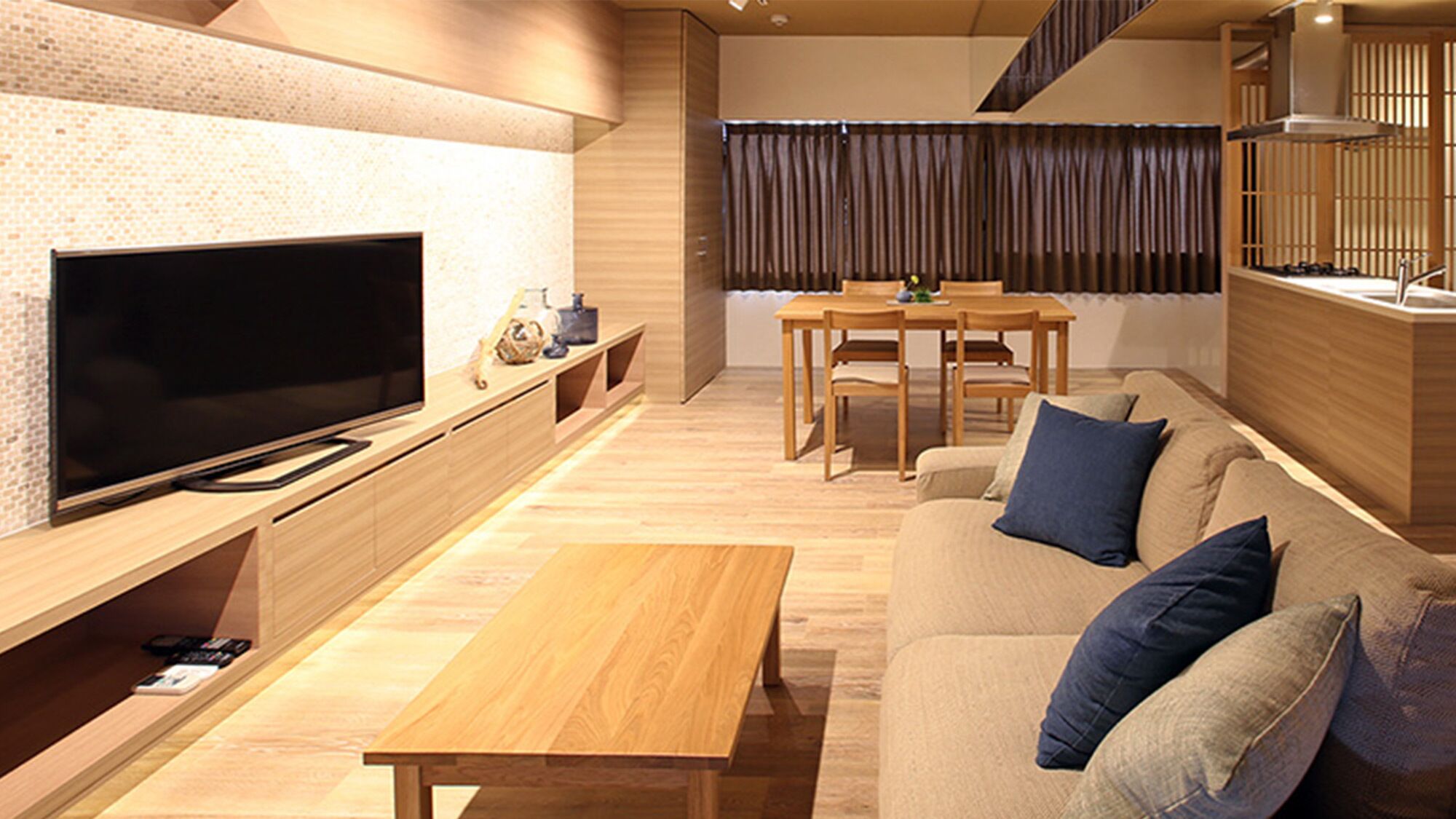 A modern living room with a flat-screen TV, wooden furniture, a dining area, and a staircase.