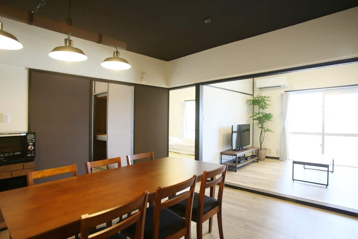 A dining area with a table and chairs, a microwave, and a television in the background.