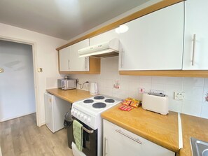 Una cocina compacta con armarios blancos, un microondas, un tostador y una estufa.
