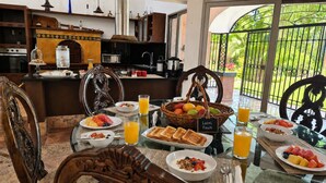 En frukostuppdukning med ett bord för två personer, med tallrikar som innehåller rostat bröd, frukt och flingor, samt glas med apelsinjuice.