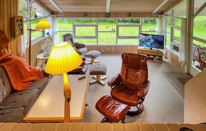 A cozy living room with a sofa, a coffee table, a leather armchair, a TV, and a window with a view of a grassy area. - Beautiful home in Fjerritslev with WiFi (Fjerritslev)