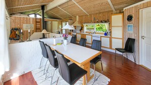 Interior acolhedor de uma cabana, com área de jantar, cozinha e uma grande janela.