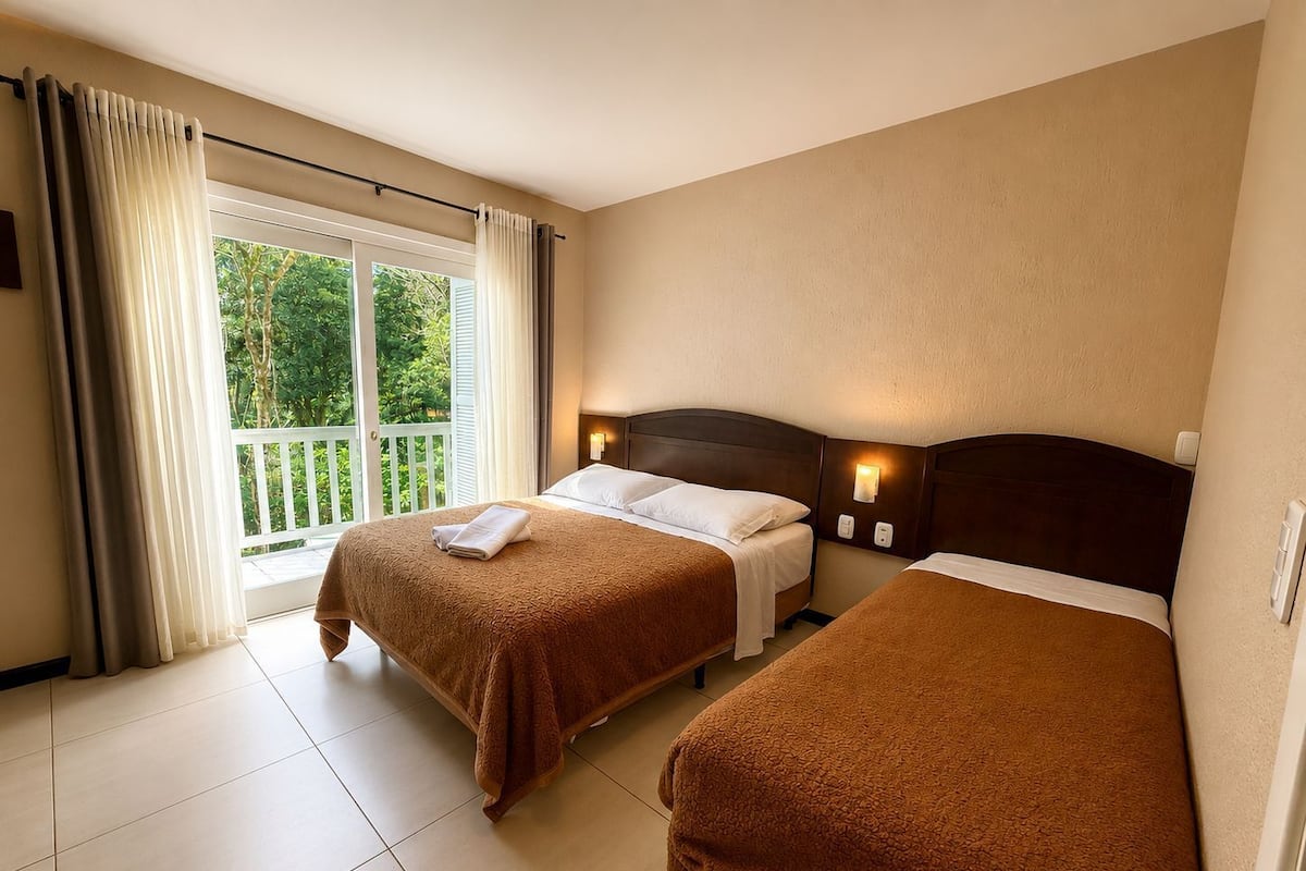 Habitación de hotel con dos camas, un balcón y vistas a zonas verdes.