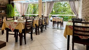 A restaurant with multiple tables, chairs, and a view of greenery outside. - Pousada nosso lar (Gramado)