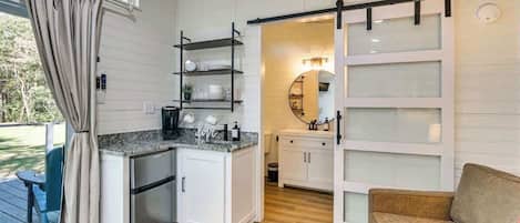 Una cocina compacta con refrigerador integrado, un comedor con mesa y sillas, y un puerta corrediza de vidrio que da a un balcón.
