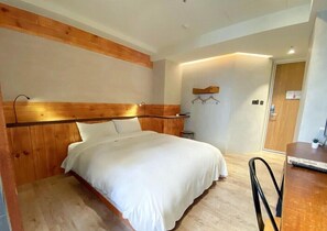 A hotel room with a wooden headboard, a bed with white linens, a desk with a chair, and a small stool. - Old School (Taichung)