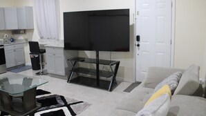 A living room with a flat-screen TV, a glass coffee table, a sofa, and a kitchen area with cabinets and a sink. - Cozy 1-bedroom apartment in perfect Covington with AC (Covington)