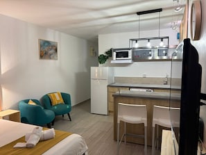 Ein kompaktes Hotelzimmer mit Bett, einer kleinen Küchenzeile, zwei Stühlen und einem Schreibtisch.