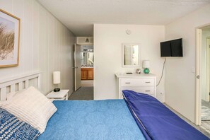 Ein Schlafzimmer mit Bett, Nachttisch, Kommode, Fernseher und einem durchgehenden Türrahmen sichtbarem Badezimmer.